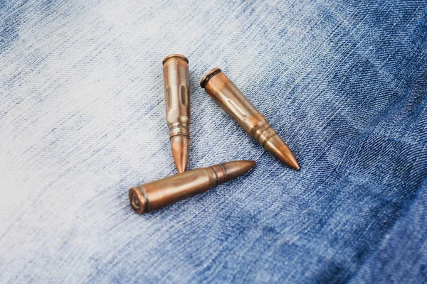 Three metal bullets for assault rifle on blue new jeans