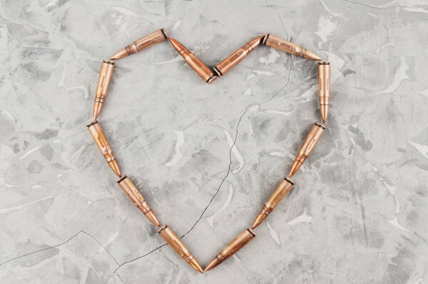 Heart laid out of metal bullets for assault rifle on old grey broken concrete