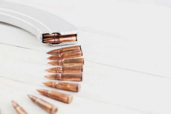 Silver full magazine for assault rifle and row of bullets on old rustic white wooden planks