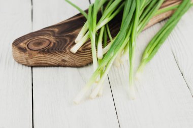 Eski beyaz rustik ahşap masa üzerinde kahverengi kesme tahtası üzerinde yeşil taze soğan bir sürü