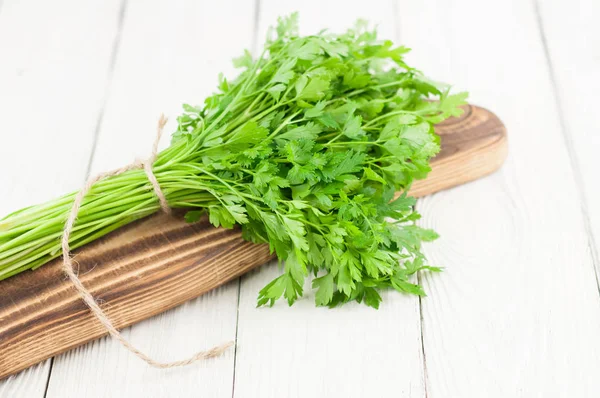 Eski beyaz ahşap rustik plakalar üzerinde kesme tahtası üzerinde kahverengi halat ile bağlı yeşil çiğ taze maydanoz Demet