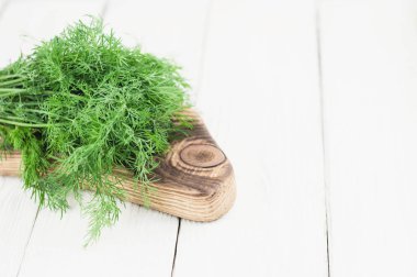 Eski ahşap beyaz rustik plakalar üzerinde kahverengi kesme tahtası üzerinde yeşil taze ham dereotu yığını