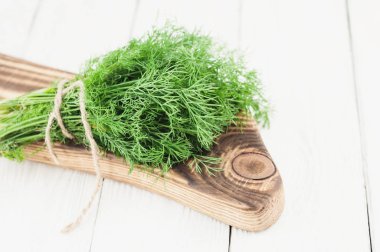 Eski ahşap beyaz rustik plakalar üzerinde ahşap kesme tahtası üzerinde kahverengi halat bağlı yeşil taze ham dereotu yığını