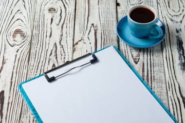 Eski rustik yıpranmış beyaz ahşap masa üzerinde boş kağıt levhalar ile plastik pano yanında siyah kahve tam mavi fincan. Metniniz için alan kopyalama