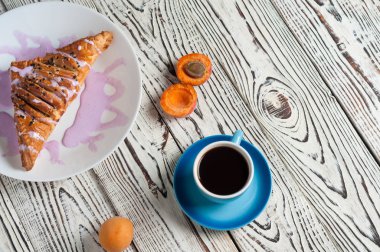 Mor krem ve kayısı ile üçgen şeklinde pişmiş tatlı topuz yakın sıcak siyah kahve tam seramik fincan beyaz yıpranmış ahşap masa üzerinde yatıyor