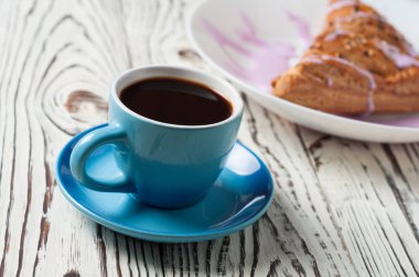 Mor krem ile üçgen şeklinde pişmiş tatlı topuz yakın sıcak siyah kahve tam seramik fincan beyaz yıpranmış ahşap masa üzerinde yatıyor