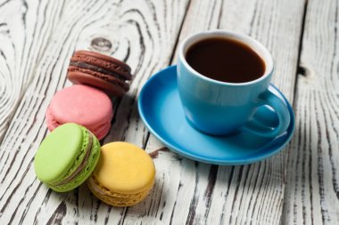 Eski yıpranmış rustik beyaz masa üzerinde dağınık tatlı macaroons yakın sıcak siyah kahve tam seramik fincan