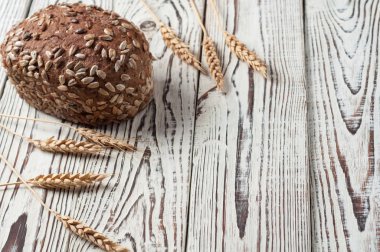 Buğday başakçık yakın Ayçiçeği tohumları ile çavdar ekmeği bir bütün somun eski yıpranmış Beyaz ahşap masada yatıyor