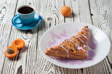 Mor krem ve kayısı ile üçgen şeklinde pişmiş tatlı topuz yakın sıcak siyah kahve tam seramik fincan beyaz yıpranmış ahşap masa üzerinde yatıyor