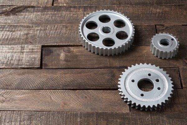 Three metal silver gears lies on old weathered wooden table in workshop. Copy space for text