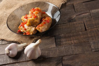 Çuvallama ve rustik ahşap masa üzerinde sarımsak yakın siyah cam tabakta pirinç ve et dolu domates soslu haşlanmış lahana rulo bir porsiyon