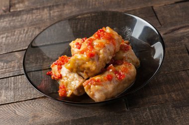 Rustik ahşap masada siyah cam tabakta pirinç ve et dolu domates soslu haşlanmış lahana rulo bir porsiyon