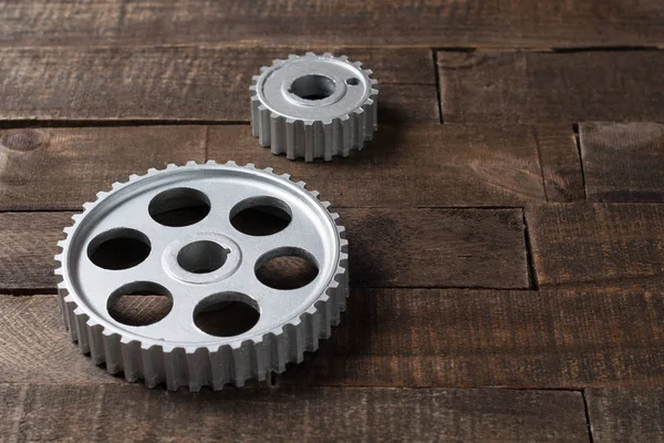 Two metal silver gears lies on old weathered wooden table in workshop. Copy space for text