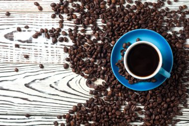 Eski rustik beyaz ahşap masada dağınık kızarmış fasulye çok yakın siyah sıcak kahve tam mavi seramik fincan. Metin için boşluk Kopyala