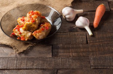 Sarımsak, çuvallama ve rustik ahşap masa nın yanında siyah cam tabakta pirinç ve et dolu domates soslu haşlanmış lahana rulobir porsiyon