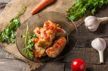 Çuvallama ve rustik ahşap masa üzerinde sebze yakın siyah cam tabakta pirinç ve et dolu domates soslu haşlanmış lahana rulo bir porsiyon