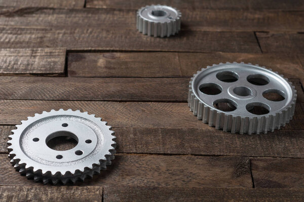 Three metal silver gears lies on old weathered wooden table in workshop. Copy space for text