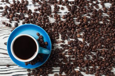 Eski rustik beyaz ahşap masa üzerinde dağınık kızarmış fasulye çok yakın siyah sıcak kahve Tam mavi seramik fincan