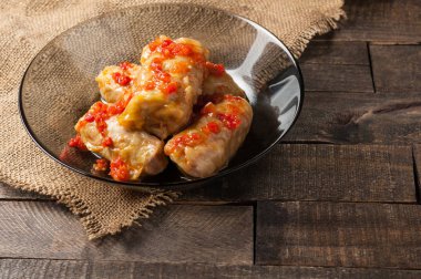 Çuvallama ve rustik ahşap masa üzerinde siyah cam tabakta pirinç ve et dolu domates soslu haşlanmış lahana rulo bir porsiyon