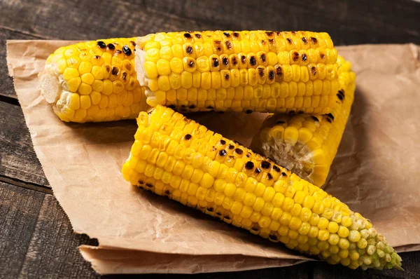 Heap of fried corn cobs lies on crumpled paper and old brown rustic wooden table