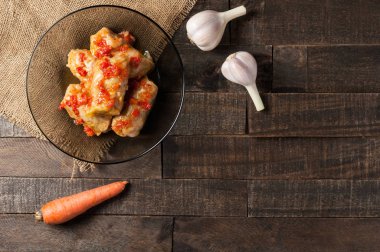 Sarımsak, çuvallama ve rustik ahşap masa nın yanında siyah cam tabakta pirinç ve et dolu domates soslu haşlanmış lahana rulobir porsiyon