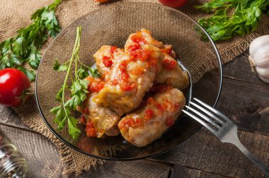 Çuvallama ve rustik ahşap masa üzerinde sebze yakın metal çatal ile siyah cam tabakta pirinç ve et dolu haşlanmış lahana rulo bir porsiyon