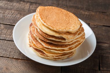 Kremasız ev yapımı krep yığını yuvarlak beyaz seramik plaka ve eski rustik ahşap masa üzerinde yatıyor