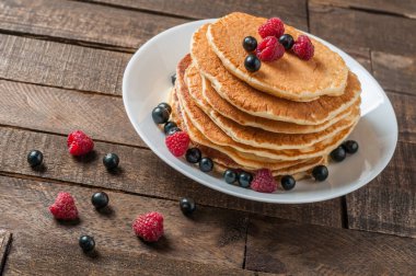 Taze ahududu ile ev yapımı krep yığını, frenk üzümü yuvarlak beyaz seramik plaka ve eski rustik ahşap masa yatıyor