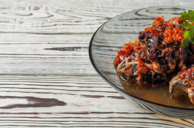 Koyu cam kase içinde eritilmiş peynir ve domates sosu ile pişmiş dolgulu patlıcan rustik beyaz ahşap masa üzerinde yatıyor. Kopyalama alanı