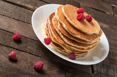 Taze ahududu ile ev yapımı krep yığını yuvarlak beyaz seramik plaka ve eski rustik ahşap masa yatıyor