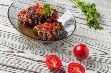 Taze domates ve maydanoz yakın koyu cam kase içinde eritilmiş peynir ve sos ile pişmiş dolgulu patlıcan rustik beyaz ahşap masa üzerinde yatıyor