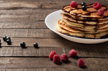 Çikolata krema, ahududu, frenk üzümü ile ev yapımı krep yığını yuvarlak beyaz seramik plaka ve eski rustik ahşap masa yatıyor. Metin için alan kopyalama