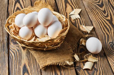 Çuval bezi üzerinde talaş ile sepette tavuk yumurtası seti rustik ahşap masa üzerinde yatıyor