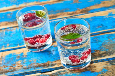 Yaprak ve çilek ile içecekler dolu iki şeffaf bardak yıpranmış mavi ahşap masa üzerinde yatıyor