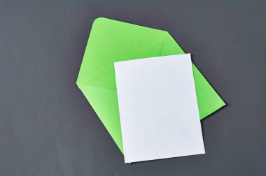 Yeşil açık kare zarf ın yanında boş beyaz kağıt levha eski çizik koyu beton yatıyor. Metin için alan