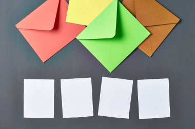 Beyaz boş kağıt levhalar yanında renkli kare zarflar grubu eski çizik koyu beton yatıyor. Metin için alan