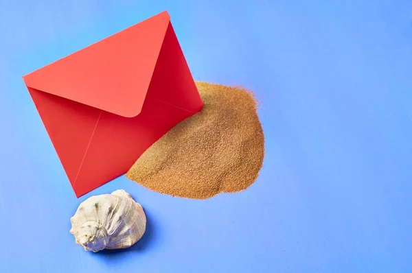 红纸信封 贝壳和一堆干沙在蓝色划伤的混凝土 文本空间 — 图库照片