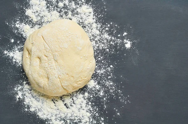Ball of dough with flour lies on dark concrete table. Baking process. Copy space. Top view