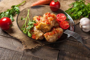 Çuvallama ve rustik ahşap masa üzerinde sebze yakın metal çatal ile siyah cam tabakta pirinç ve et dolu haşlanmış lahana rulo bir porsiyon