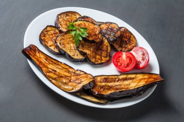 Beyaz seramik plaka ızgara patlıcan süslenmiş domates ve maydanoz dilimleri dolu çizik koyu beton yatıyor