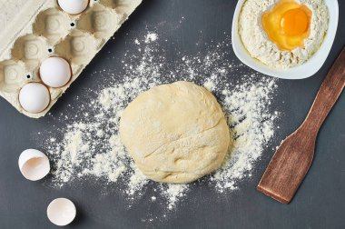 Kase ve diğer mutfak eşyaları sarısı ile kırık yumurta yakın un ile Hamur, malzemeler koyu beton masa üzerinde yatıyor. Pişirme işlemi. Üstte görüntü