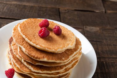Taze ahududu ile ev yapımı krep yığını yuvarlak beyaz seramik plaka ve eski rustik ahşap masa yatıyor. Metin için alan kopyalama
