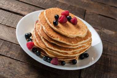 Taze ahududu ile ev yapımı krep yığını, frenk üzümü yuvarlak beyaz seramik plaka ve eski rustik ahşap masa yatıyor
