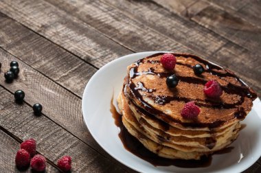 Çikolata krema, ahududu, frenk üzümü ile ev yapımı krep yığını yuvarlak beyaz seramik plaka ve eski rustik ahşap masa yatıyor. Metin için alan kopyalama