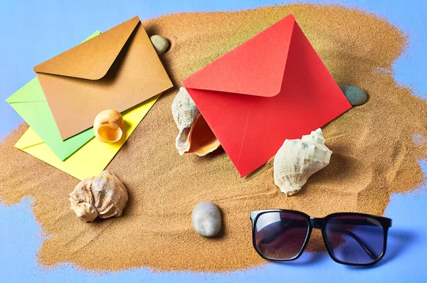 Seashells, stones, paper envelopes, black sunglasses and scattered dry sand on blue scratched concrete