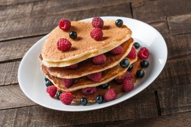 Taze ahududu ile ev yapımı krep yığını, frenk üzümü yuvarlak beyaz seramik plaka ve eski rustik ahşap masa yatıyor