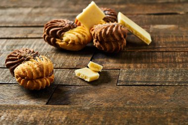 Eski rustik masada beyaz gözenekli çikolata parçaları yakınında krem ve haşhaş ile Dağınık çift renkli kurabiye. Metin için alan