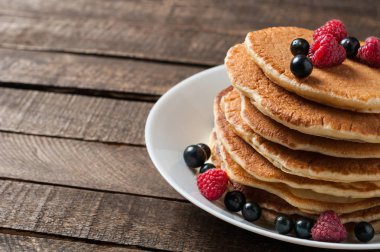 Taze ahududu ile ev yapımı krep yığını, frenk üzümü yuvarlak beyaz seramik plaka ve eski rustik ahşap masa yatıyor. Metin için alan kopyalama