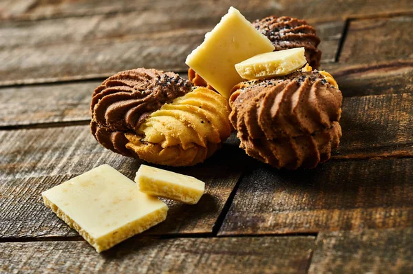 Eski rustik masada beyaz gözenekli çikolata parçaları yanında krem ve haşhaş ile Dağınık çift renkli kurabiye