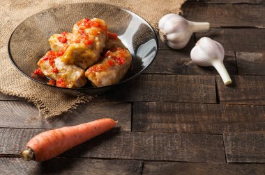 Sarımsak, çuvallama ve rustik ahşap masa nın yanında siyah cam tabakta pirinç ve et dolu domates soslu haşlanmış lahana rulobir porsiyon